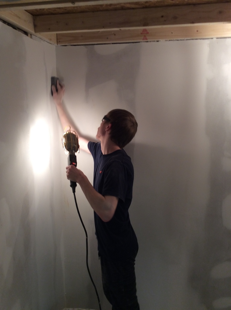 A student holds a handheld lamp and spreads plaster on drywall.