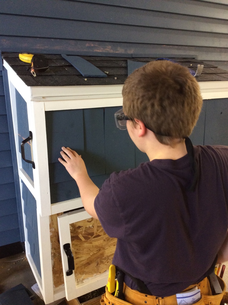 A student installs blue cedar shakes on a propane box.